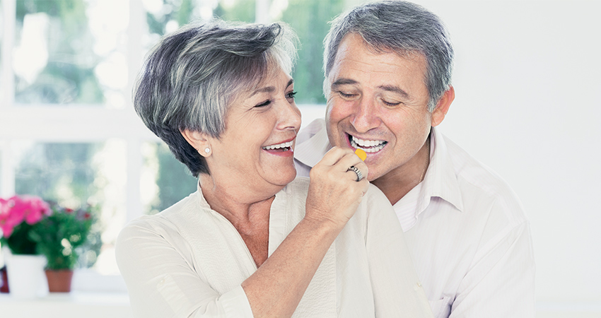 middle aged couple laughing while the woman feeds a man a gummy candy.