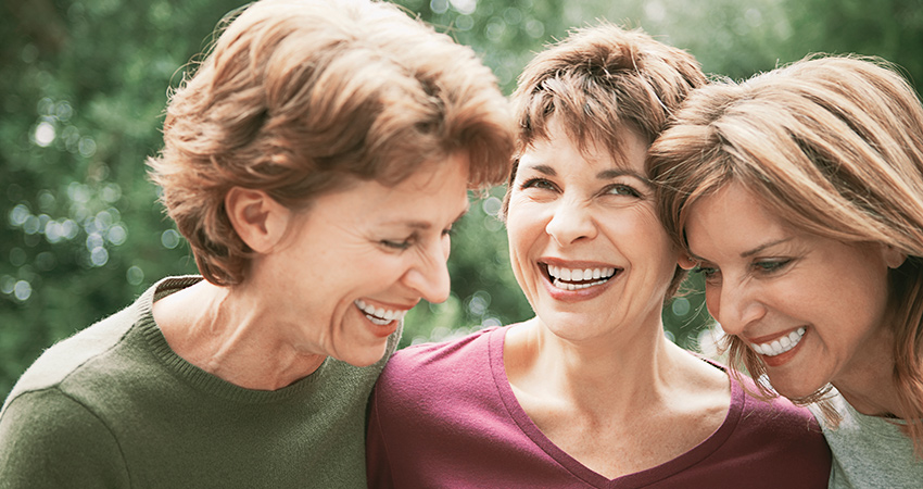 Three middle-aged women with dental implants smile